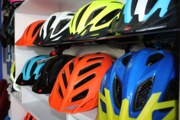 Fahrradhelme der Marke MET in vielen fröhlichen Farben liegen in einem Regal.